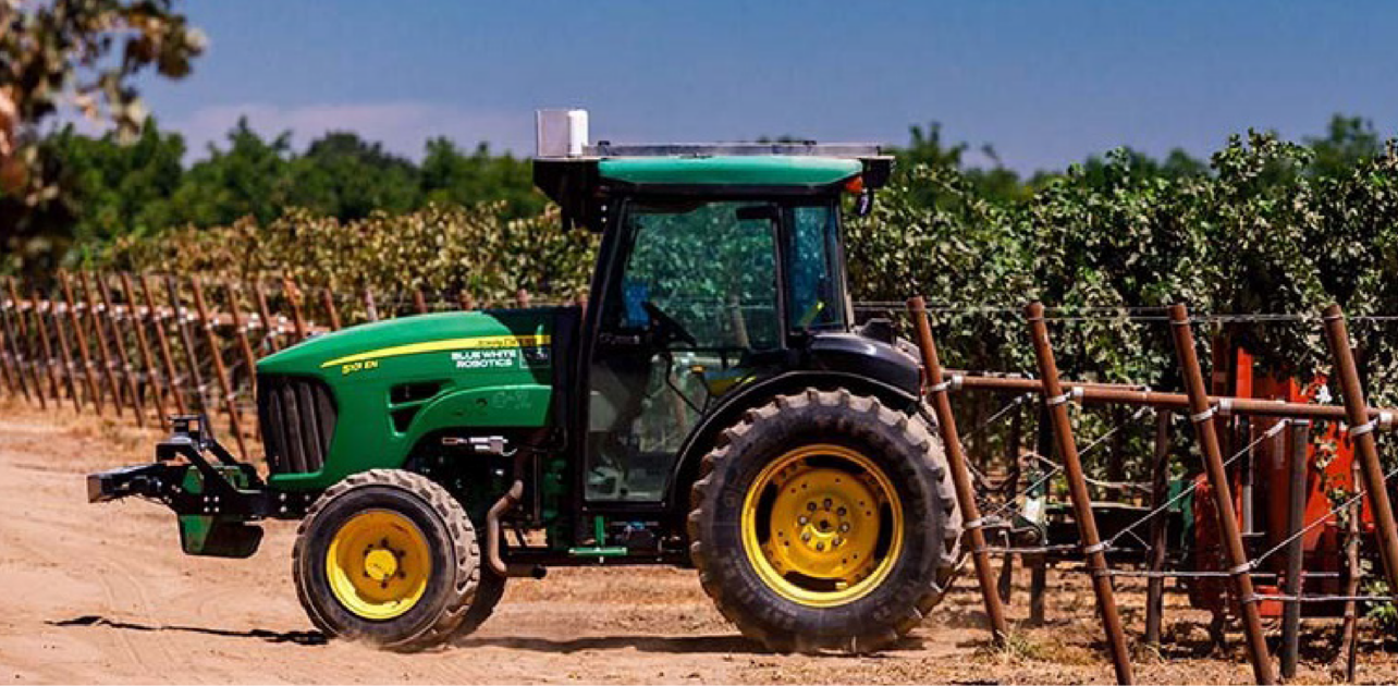 A green tractor driving down a dirt road.